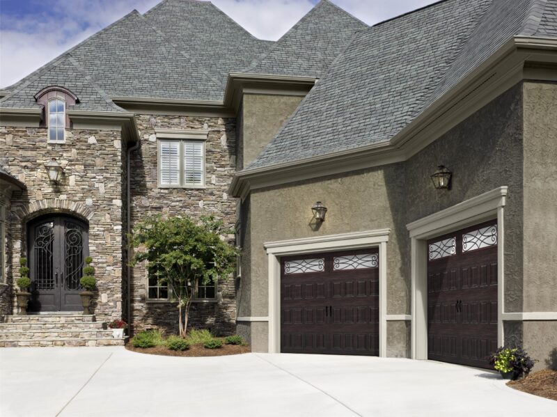 large stone house in san antonio with two dark brown garage doors with white decorative windows on the top row