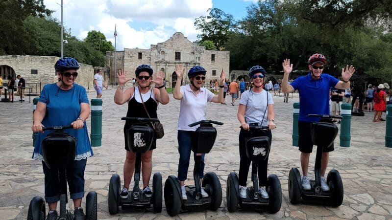 group of people wearing helmets and riding segways while posing in front of the alamo