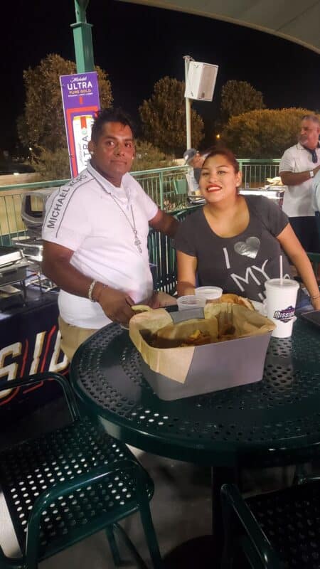 two people smiling at a camera while at a san antonio missions baseball game