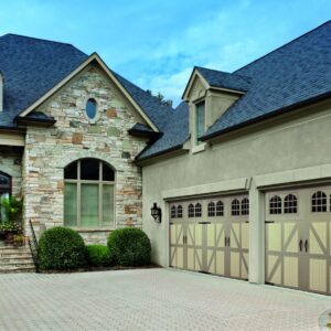 closeup of a large stone home in san anotnio with two cream amarr classica, carriage style residential garage doors with grey features