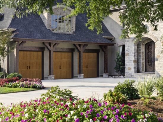 three brown faux wood grain style residential garage doors on a large stone home in san antonio