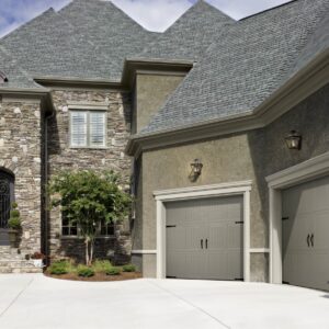large stone home in san antonio with two grey faux wood grain style residential garage doors