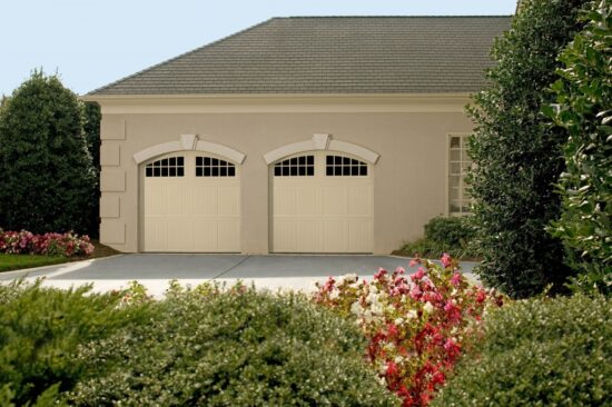 view of two cream colored amarr classica, carriage style residential garage doors with trees and grass surrounding the property