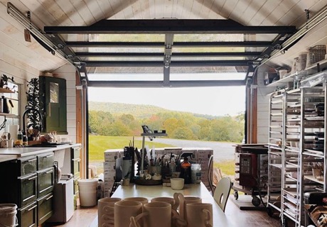 view from the inside of a pottery studio looking out through an open clopay avante AX, modern style, full-view aluminum residential garage door