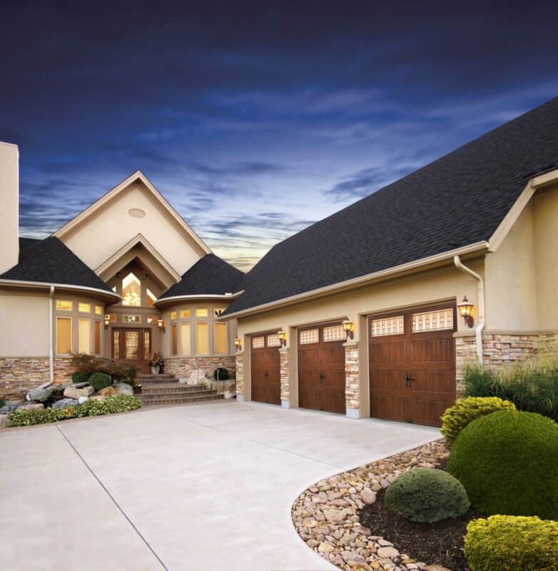 large home at dusk with three clopay gallery, faux wood grain style, residential garage doors that have vertical windows on the top row