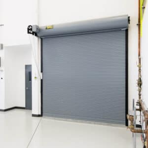 large commercial rolling fire garage door in a warehouse setting with a fire extinguisher on the wall and a smaller security garage door on the side