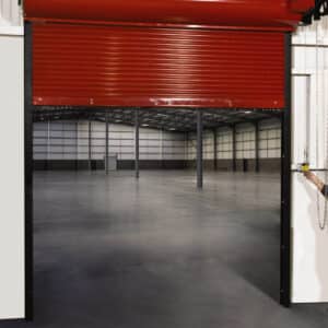 large red commercial rolling fire garage door being lifted to show an empty warehouse