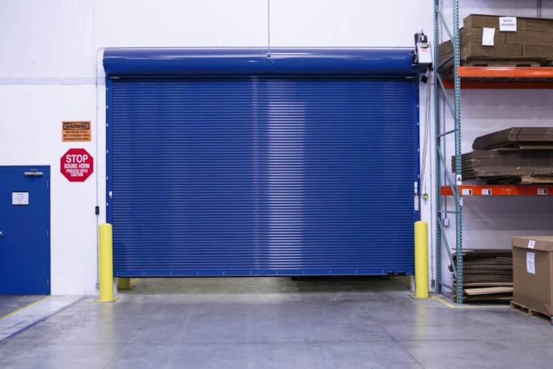 large blue commercial rolling fire garage door with a large shelf of flat boxes to the side of it in a warehouse