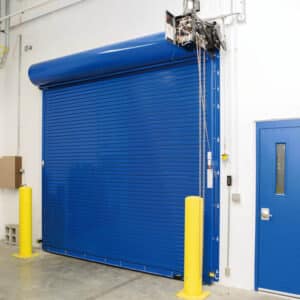 large blue commercial rolling fire garage door next to a blue door in a warehouse