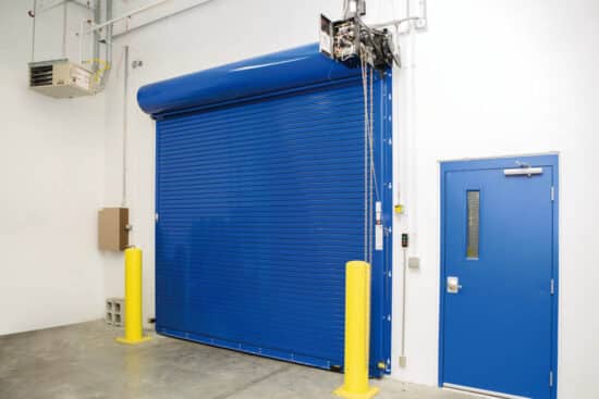 large blue commercial rolling fire garage door next to a blue door in a warehouse
