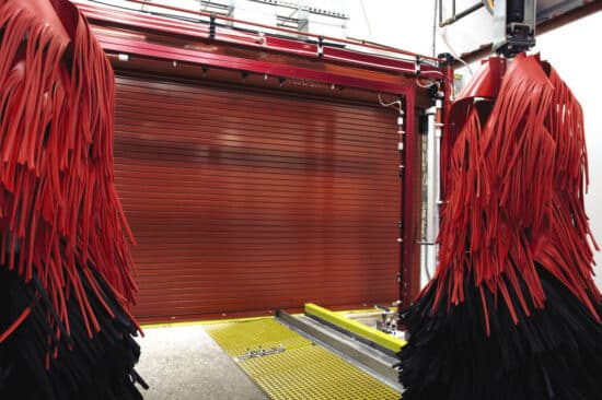large red commercial rolling door in a commercial car wash building with car wash spinning scrubbers hanging in front of it