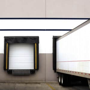 commercial sectional overhead door on a warehouse building with a large truck backed up to a loading dock and one other loading dock has no truck up next to it