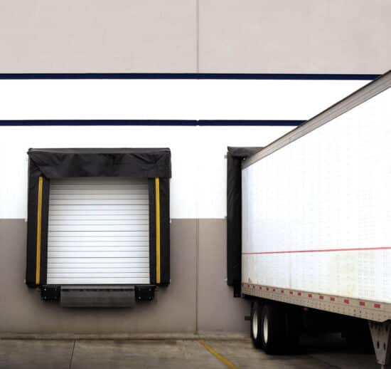 commercial sectional overhead door on a warehouse building with a large truck backed up to a loading dock and one other loading dock has no truck up next to it