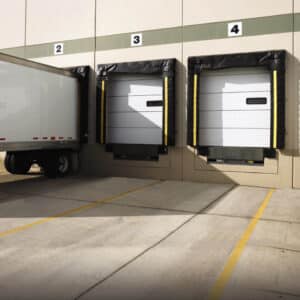 commercial garage doors in a warehouse building with a large truck backed up to a loading dock with two open loading docks