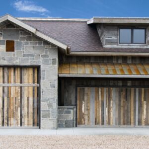 grey-toned home with two large, different sized garage doors made out of custom wood pieces, wood showing different colors