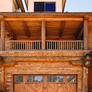 multiple story wooden home with custom wood garge door, garage door has windows on the upper parts of the door and have x-shaped pieces to add depth