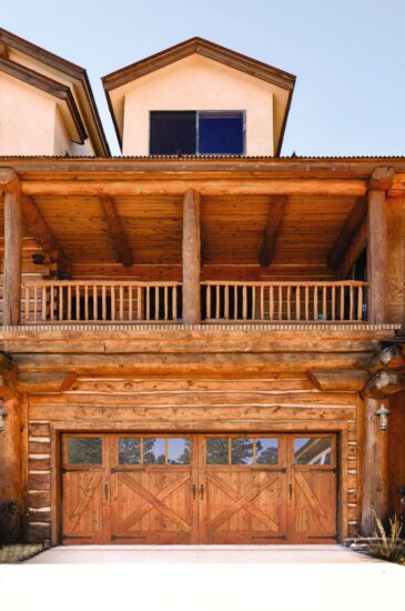 multiple story wooden home with custom wood garge door, garage door has windows on the upper parts of the door and have x-shaped pieces to add depth