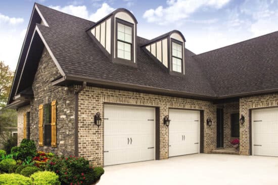 large stone home in san antonio with three cream colored carriage style, sonoma/sonoma ranch panel residential garage doors