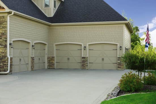 large cream colored and brick residential home with four carriage style garage doors