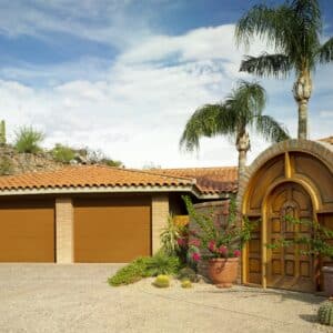 Southwestern style home with terracotta roof and three tan garage doors, complemented by a desert landscape with cacti and palm trees