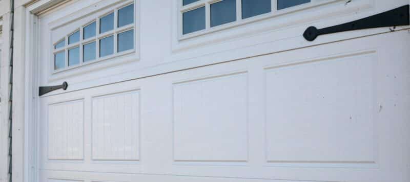 A close-up of a white garage door with decorative black hardware and small windows near the top