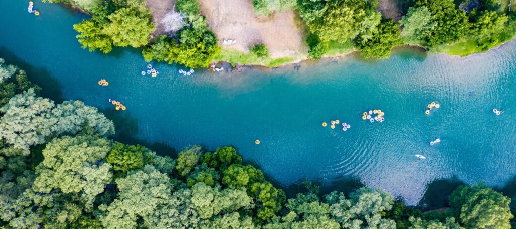 aerial view of the comal river with people floating on colorful tubes in the river surrounded by luscious green trees